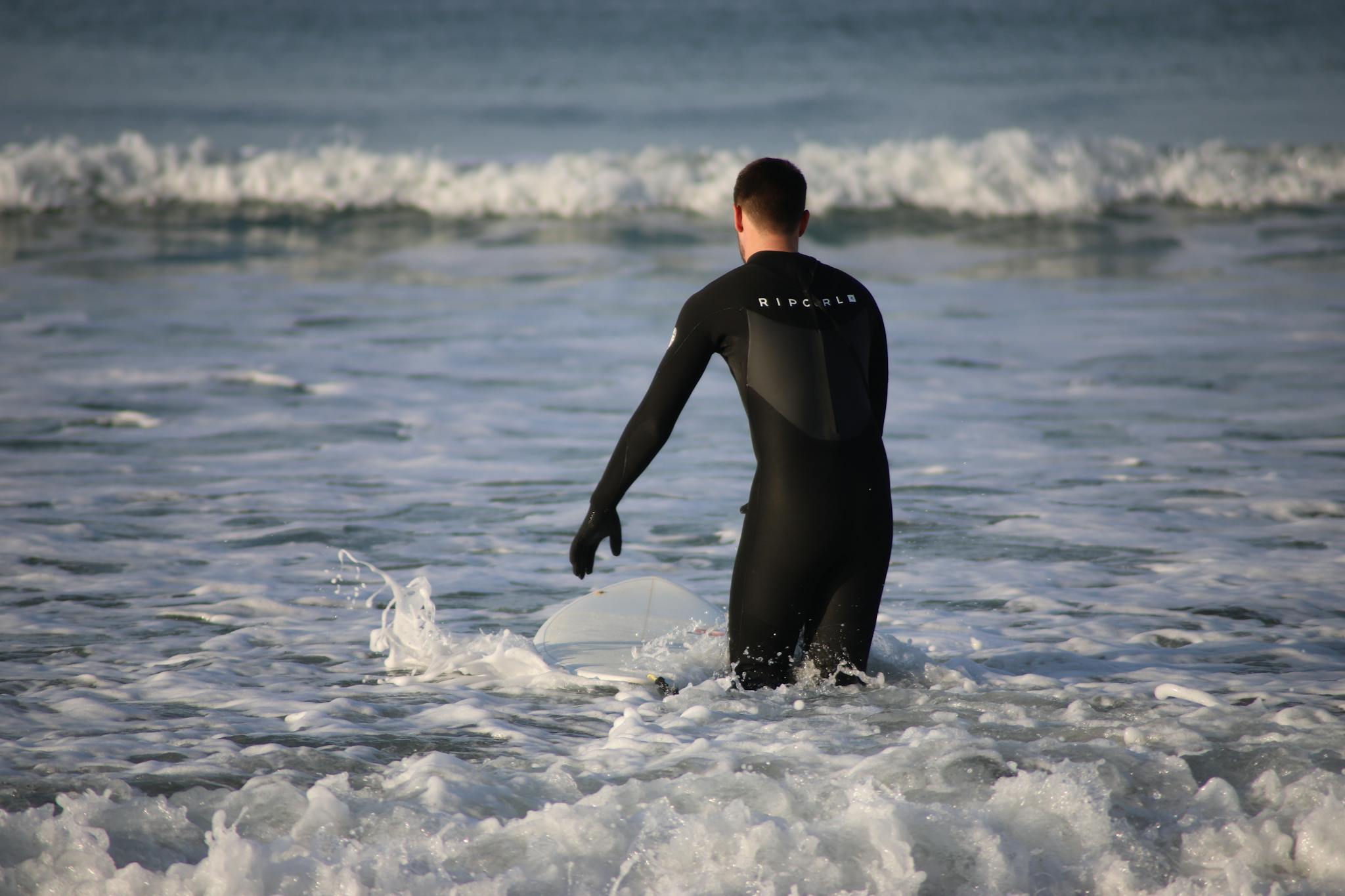 Surfer in a wetsuit prepares to ride waves on a beach in Pays de la Loire, France.